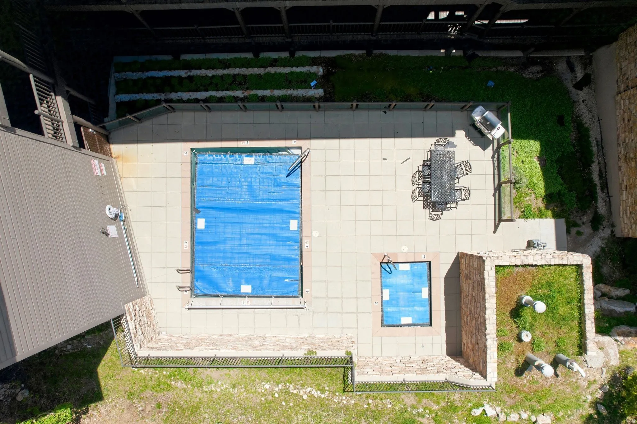 Outdoor leisure area featuring a large tiled patio, a covered rectangular pool, and a smaller covered rectangular pool