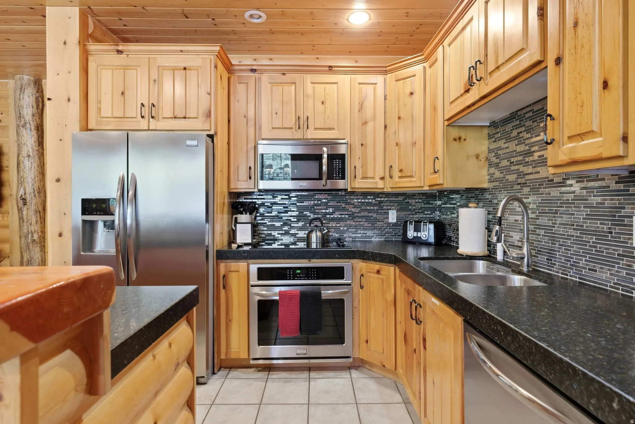 Kitchen featuring wood cabinetry, stainless steel appliances, dark countertops, a mosaic tile backsplash, and recessed lighting