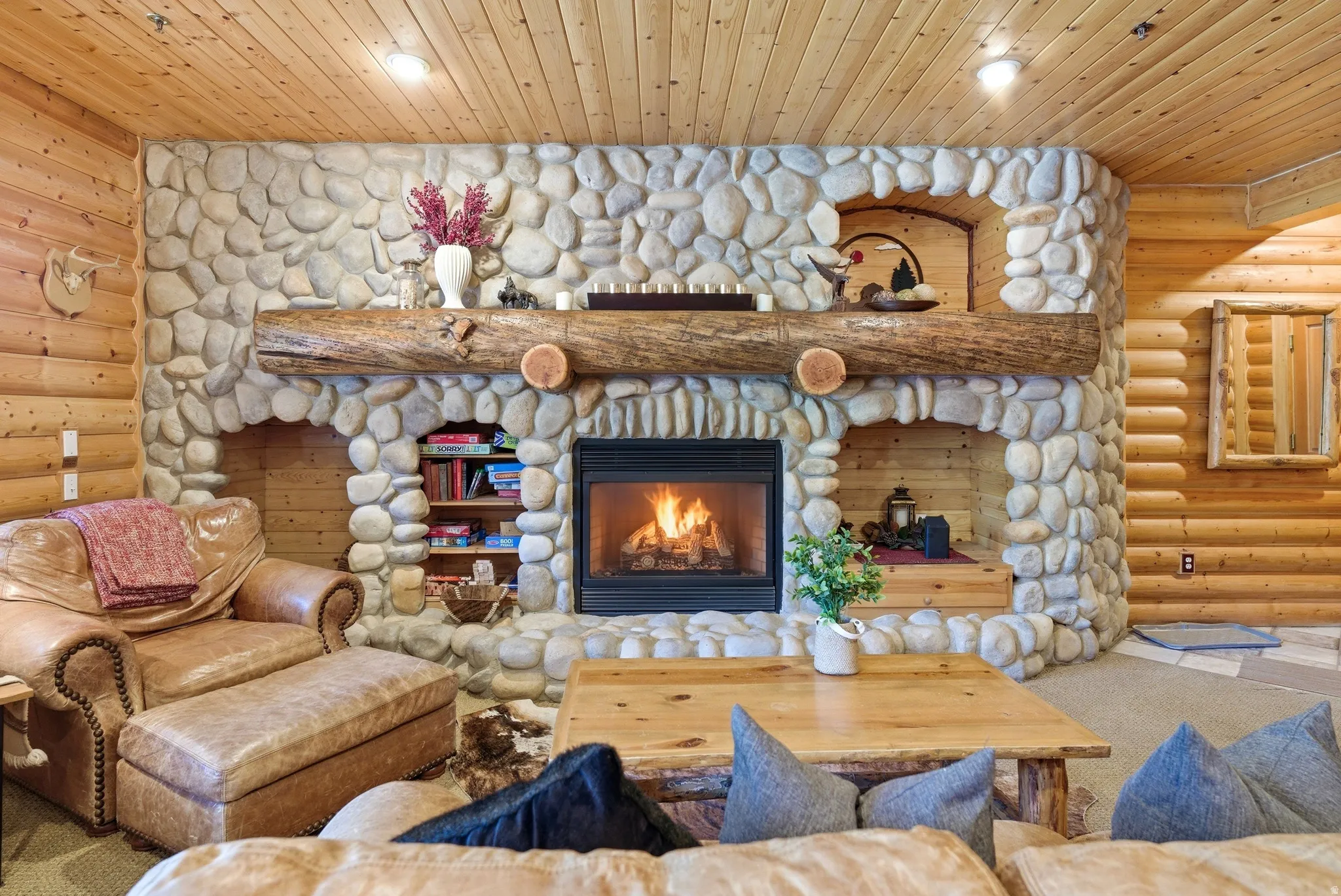 Stone fireplace with a log mantel and built-in niches, set against wood-paneled walls and a wood-finish ceiling