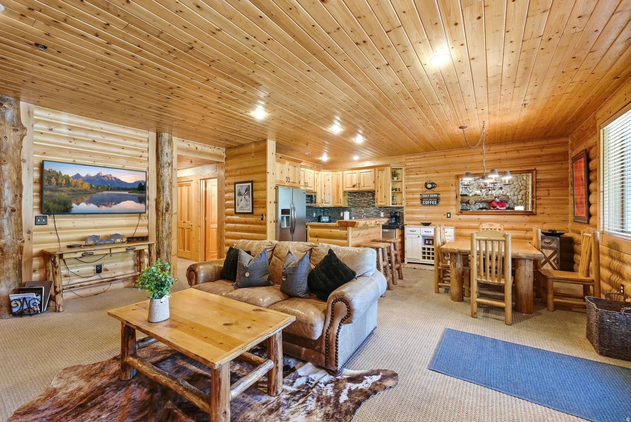 Open-concept living space featuring wood-paneled walls and ceiling, a full kitchen with stainless steel appliances, and a dining area with a wood table and chairs