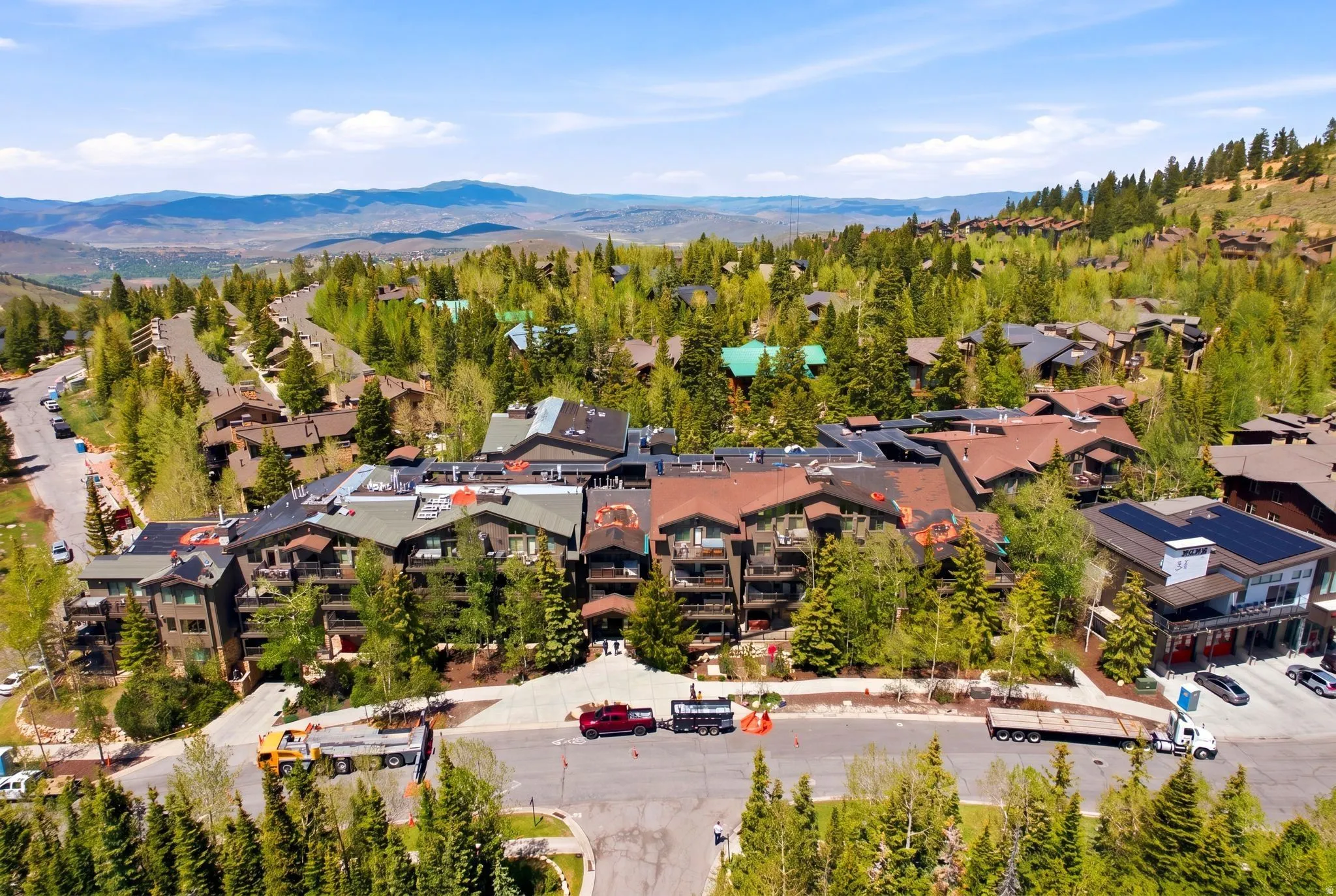 Mountain community featuring a multi-story building with balconies, surrounded by mature trees and paved roads