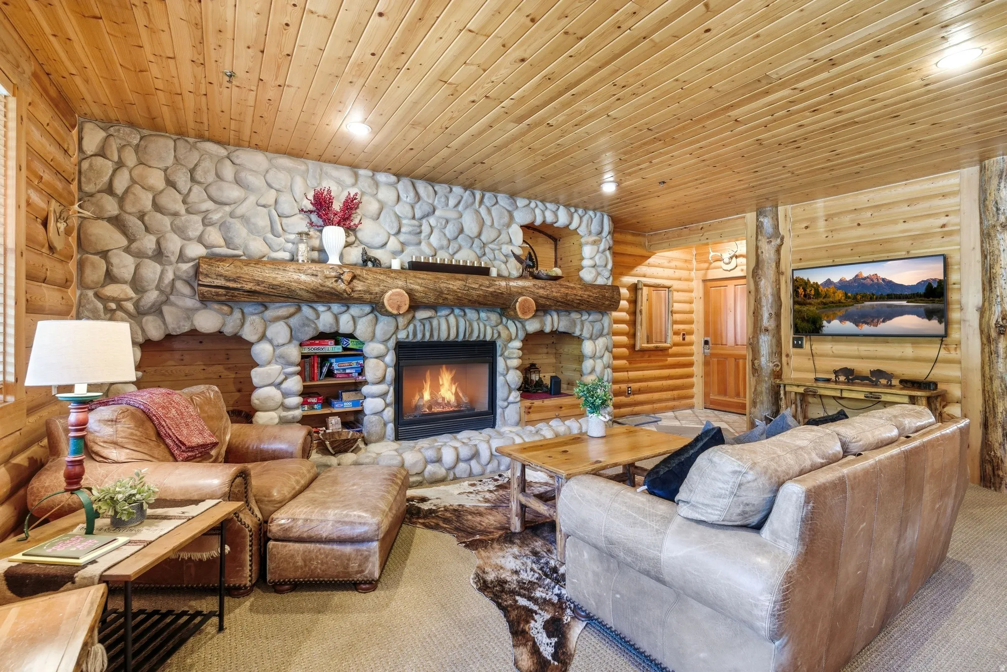 Expansive stone fireplace with a substantial log mantel, flanked by built-in shelving and a recessed hearth