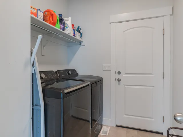 Dedicated laundry area featuring a white storage shelf, light gray walls, a paneled door with contemporary hardware, and light-toned flooring