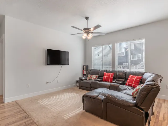 Living area featuring multiple windows with blinds, wood-finish flooring, and a ceiling fan with integrated lighting