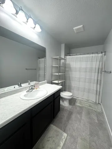Bathroom featuring a single vanity with dark cabinetry, integrated sink, and light-colored countertop