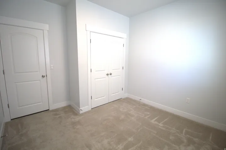 Neutral tone wall color with white trim, light-colored carpet, and bi-fold closet doors