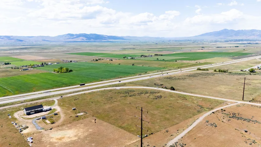 Expansive agricultural landscape featuring a prominent highway, distant mountain ranges, and scattered rural structures