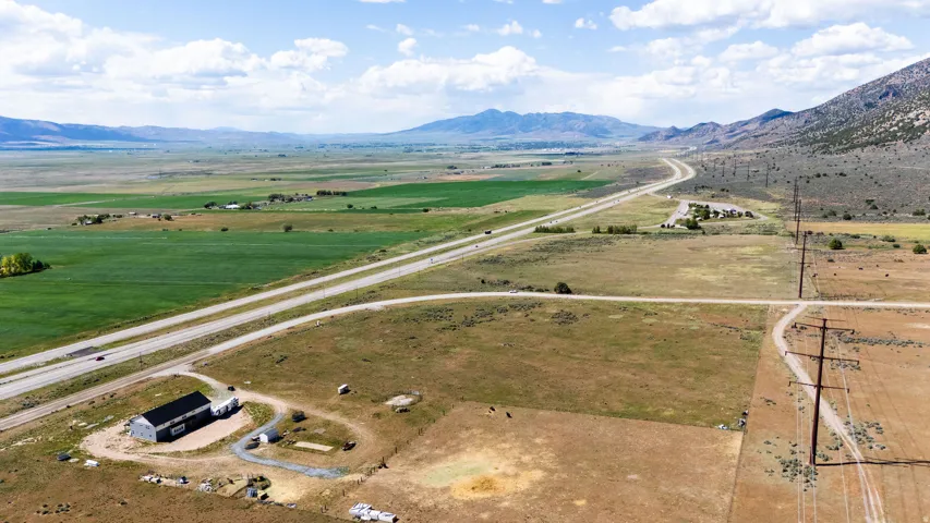 Expansive rural landscape featuring a single-story structure with a dark roof, surrounded by fields and distant mountains