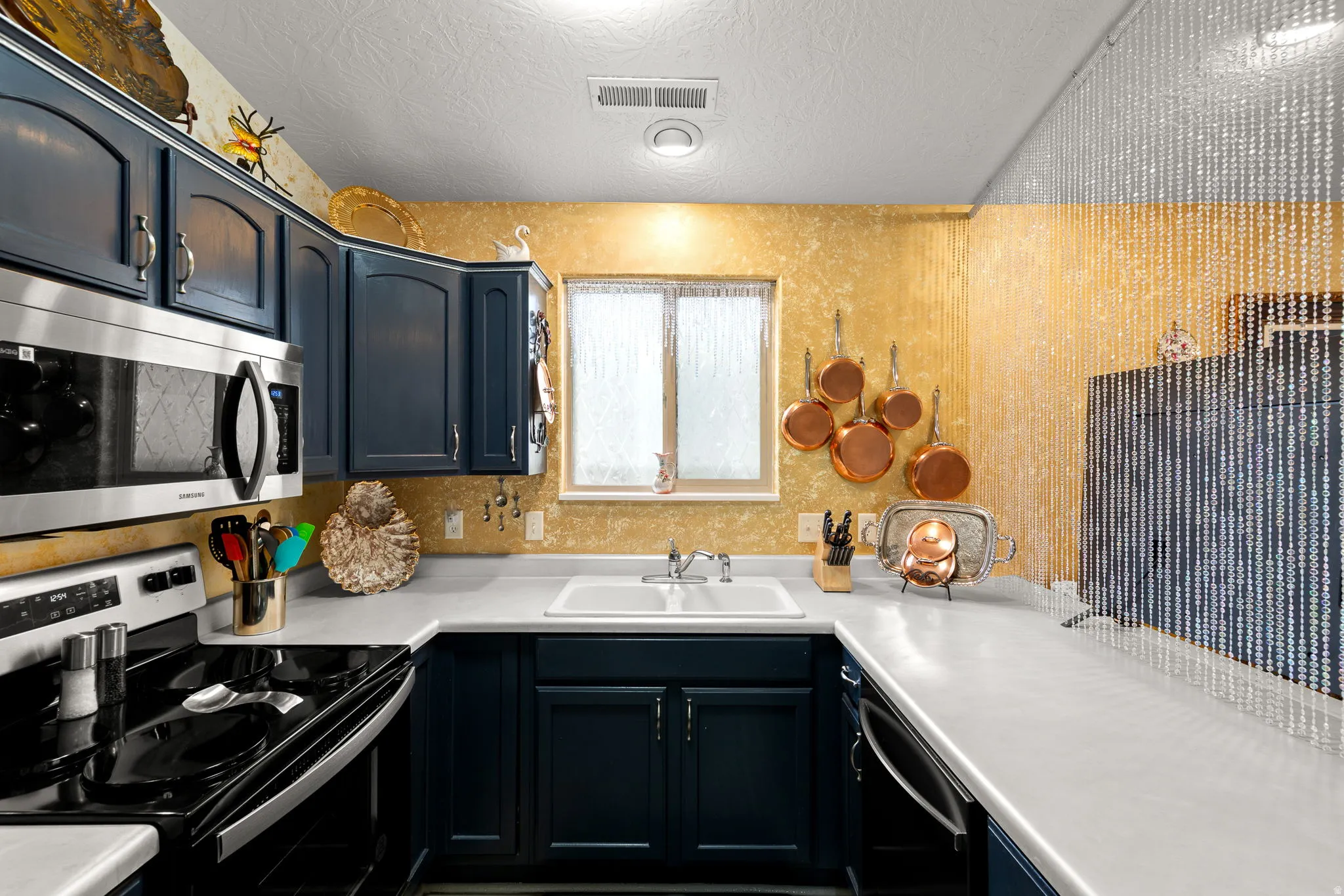 Kitchen featuring dark blue cabinetry, white countertops, stainless steel microwave, and white double-basin sink with a window above
