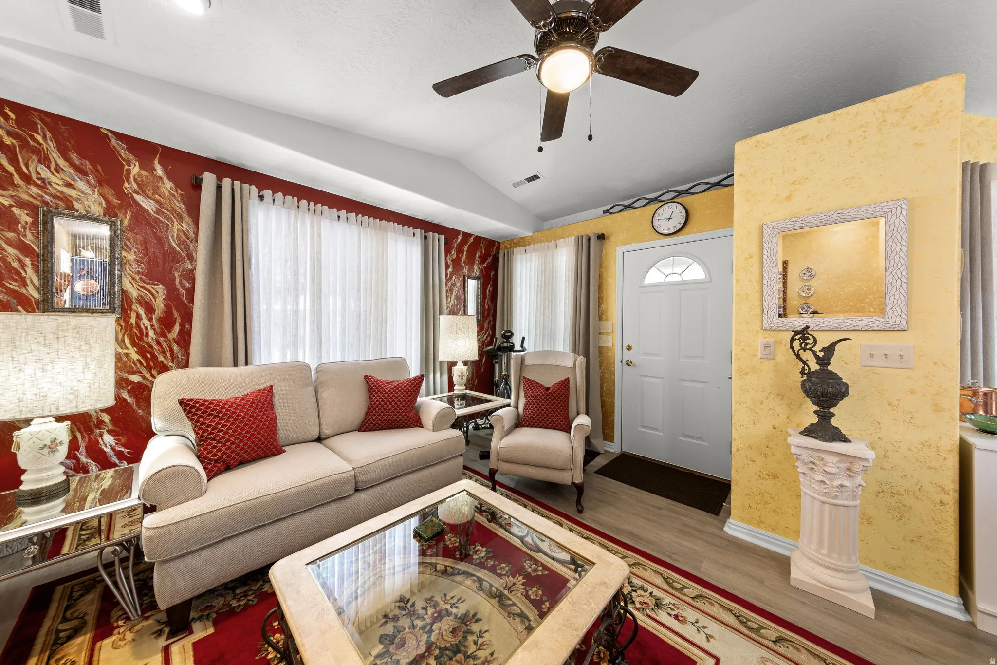 Vaulted ceiling living area with a wood-finish ceiling fan, large front door with an arched window, and light wood-finish flooring