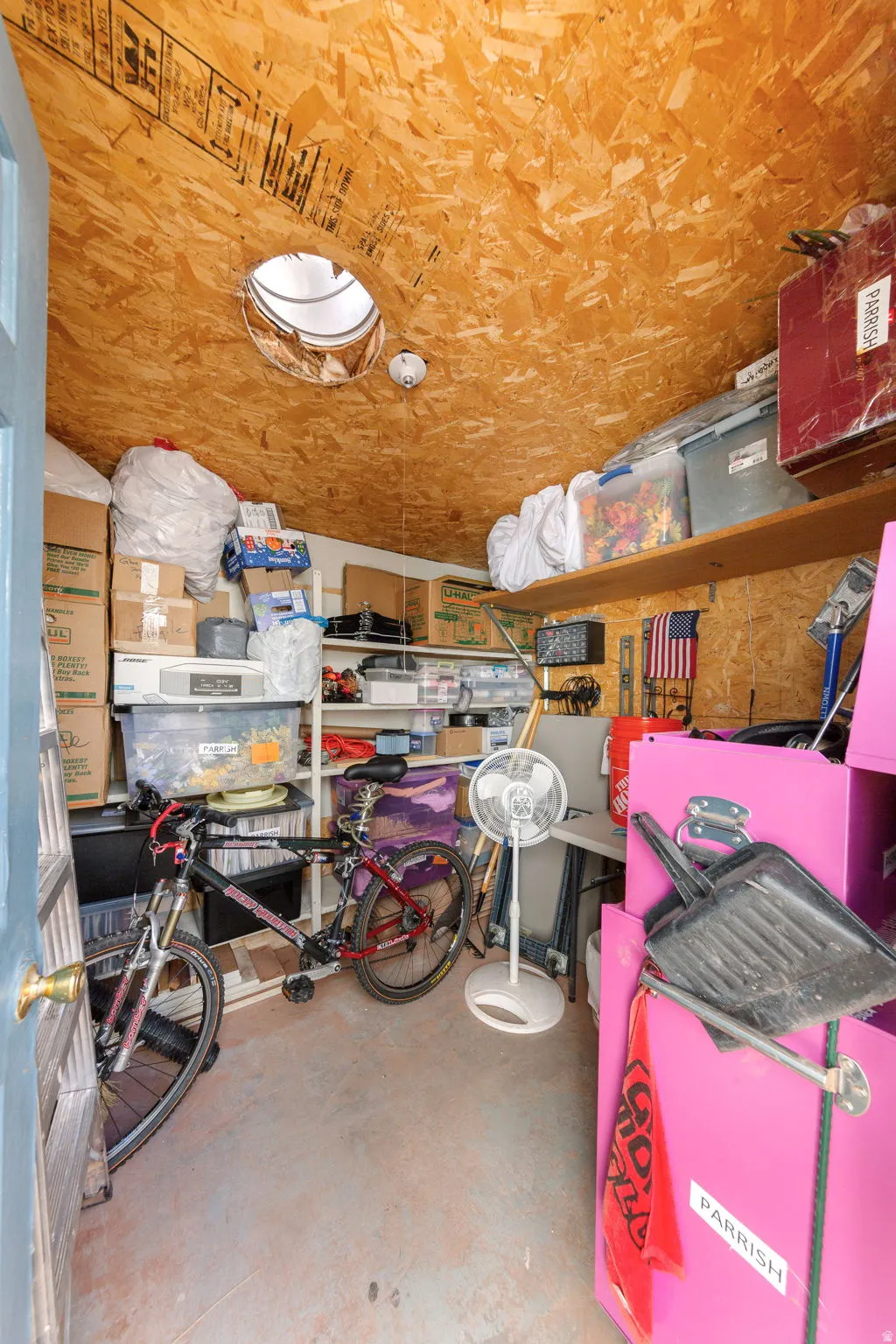 Storage space featuring exposed OSB ceiling and walls, a circular skylight, built-in shelving, concrete flooring, and a solid door