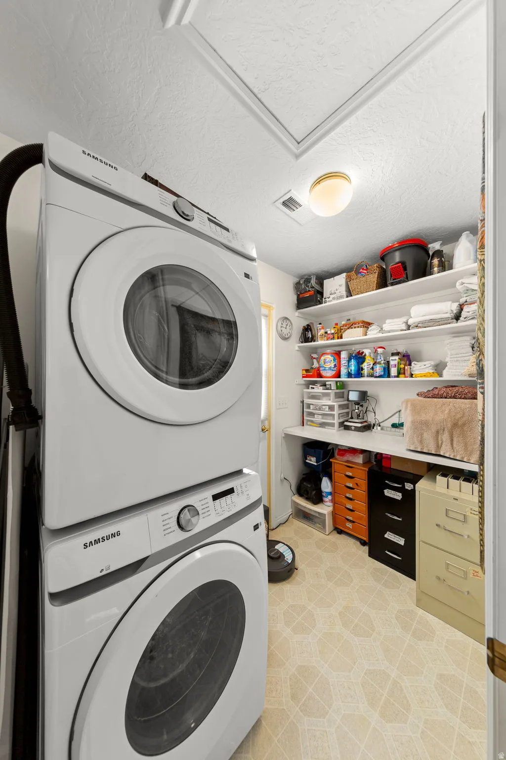 Dedicated laundry area featuring stacked appliances, overhead shelving, built-in countertop, and patterned flooring