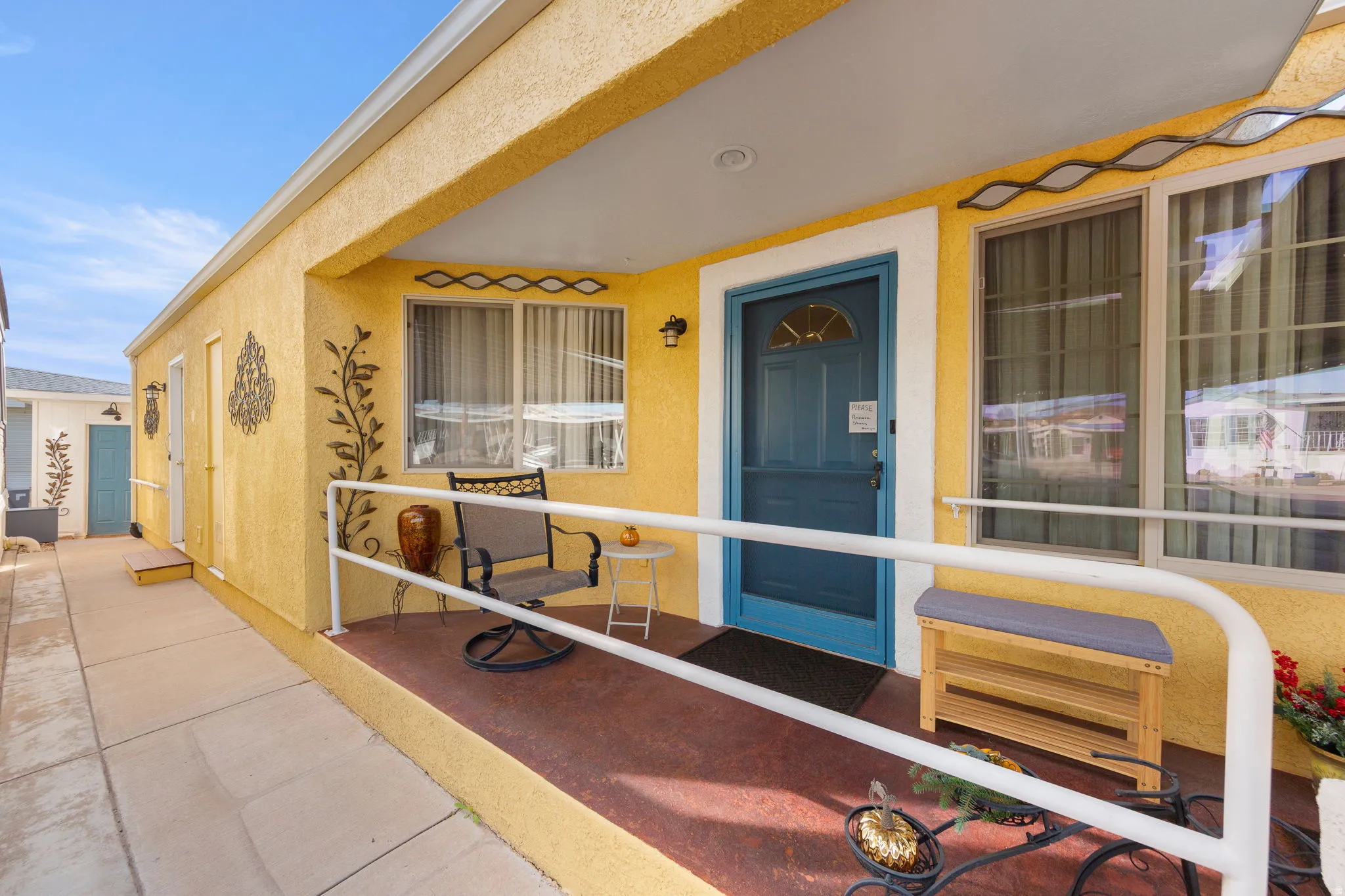 Covered entry with a bright yellow stucco exterior, a blue front door, and a white handrail