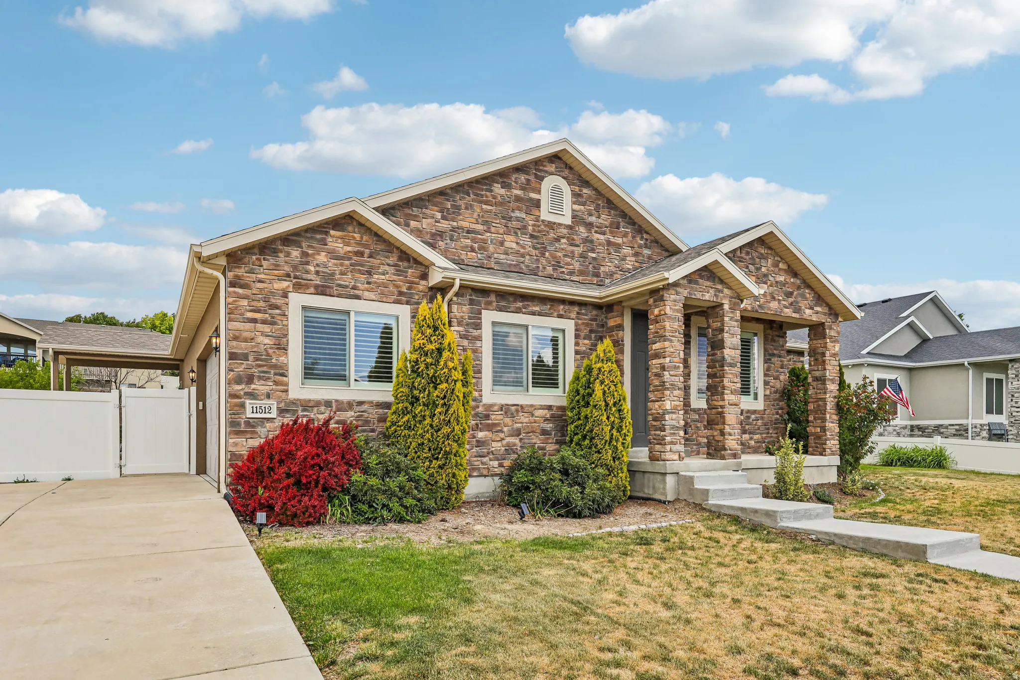 Stone veneer exterior featuring a covered front porch, concrete walkway, and attached garage