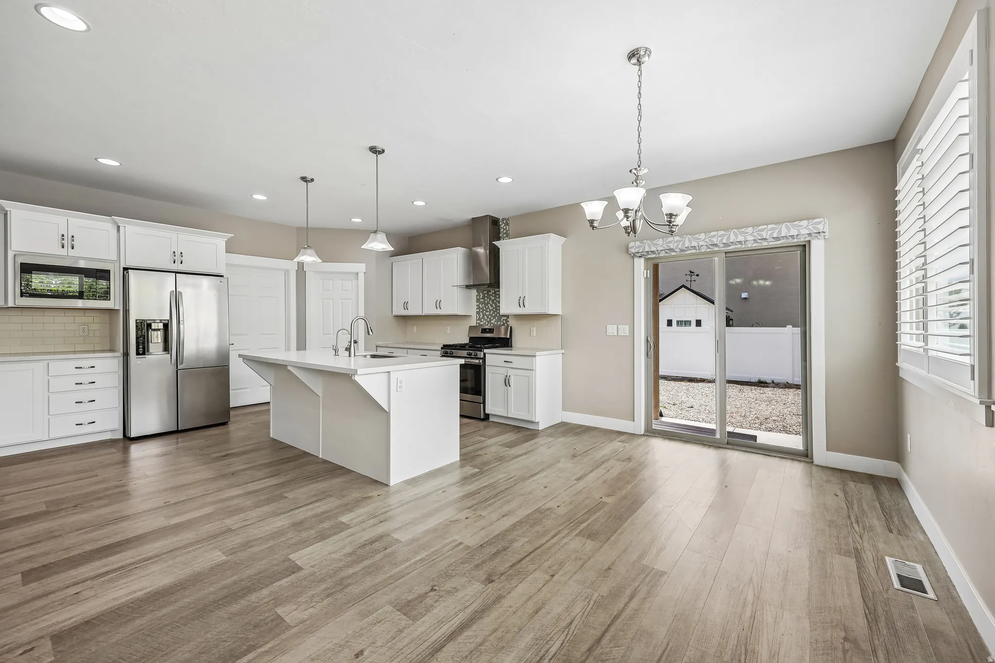 Open-concept kitchen and dining area featuring light wood-finish flooring, white cabinetry, stainless steel appliances, a center island with a sink, and a sliding glass door