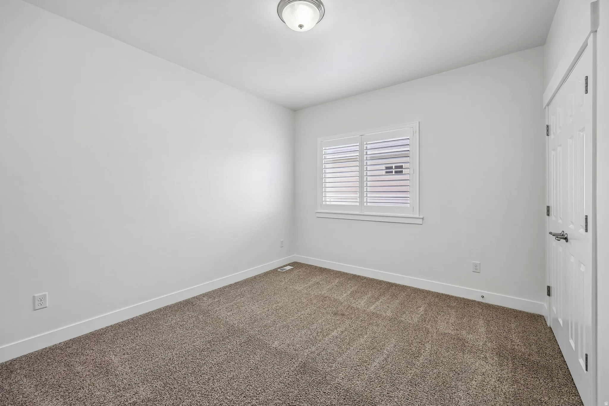 Carpeted room featuring a window with white plantation shutters, white trim, a flush mount ceiling light, and a paneled interior door
