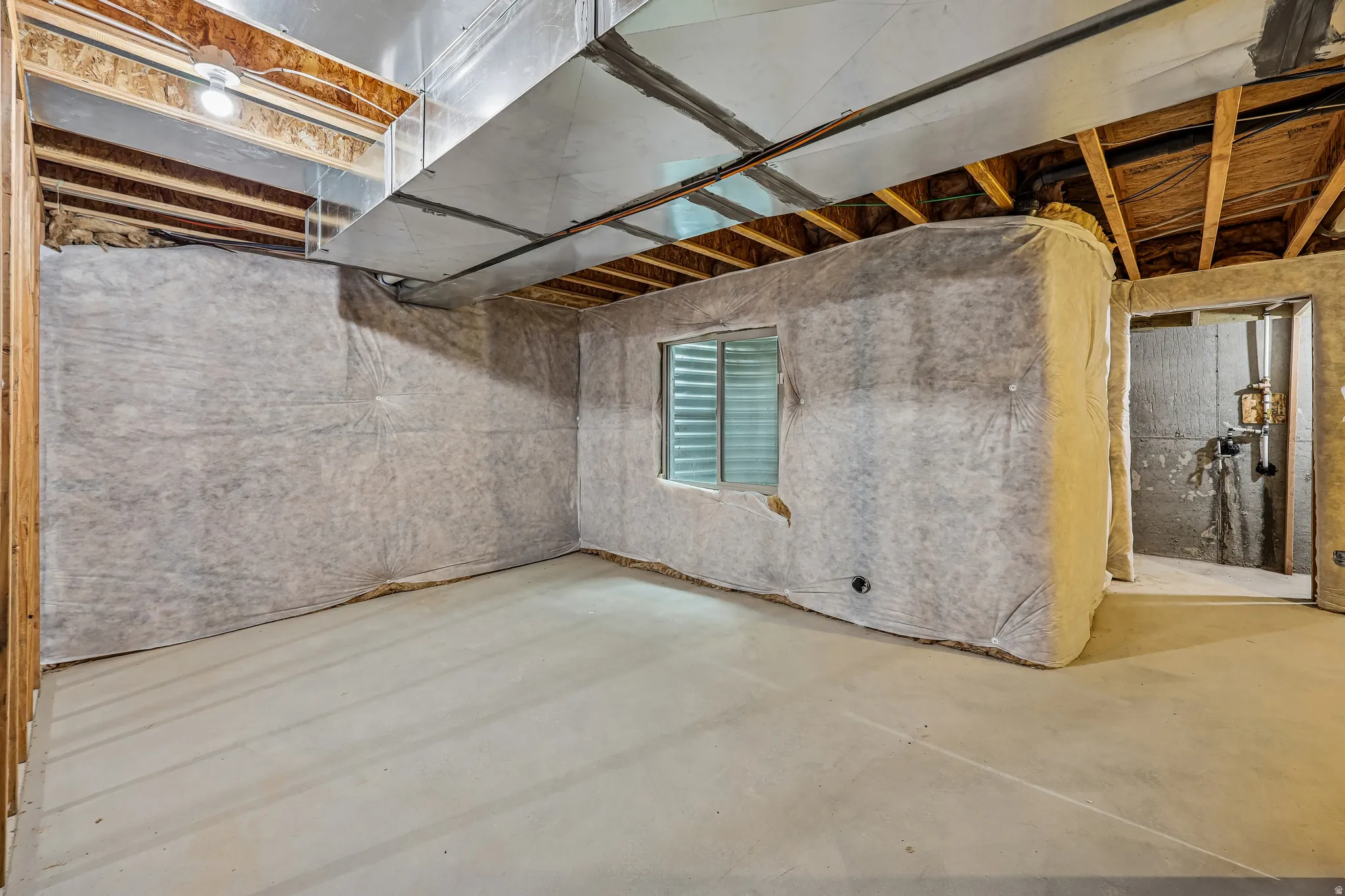 Unfinished basement space featuring exposed wood joists, a window with horizontal blinds, and a concrete floor