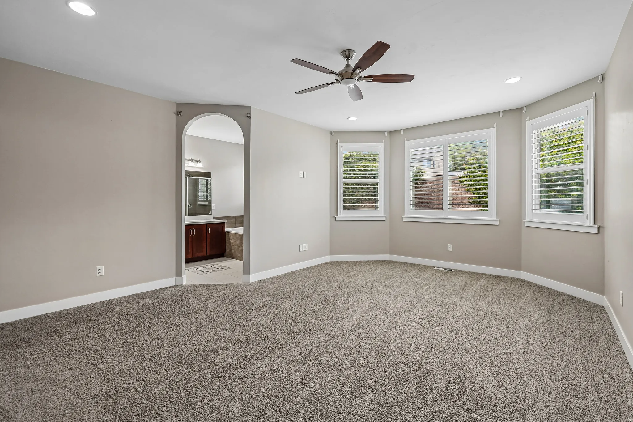 Carpeted room featuring a ceiling fan with integrated lighting, recessed ceiling lights, and multiple windows with plantation shutters