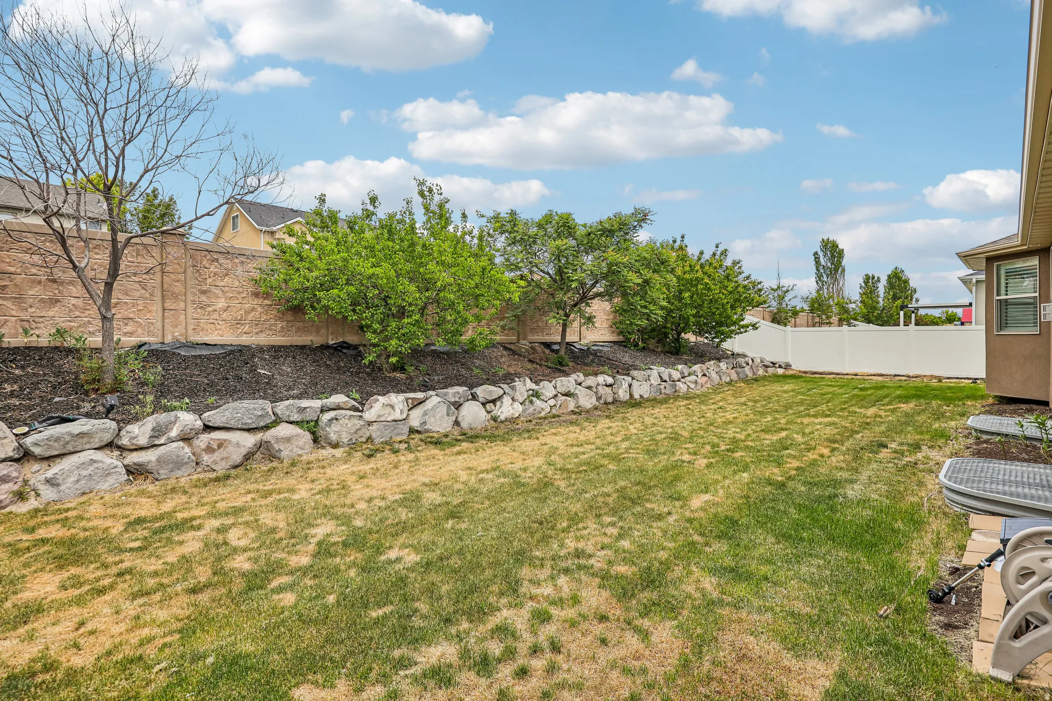 Expansive backyard featuring a rock retaining wall, mature trees, and a decorative concrete privacy fence
