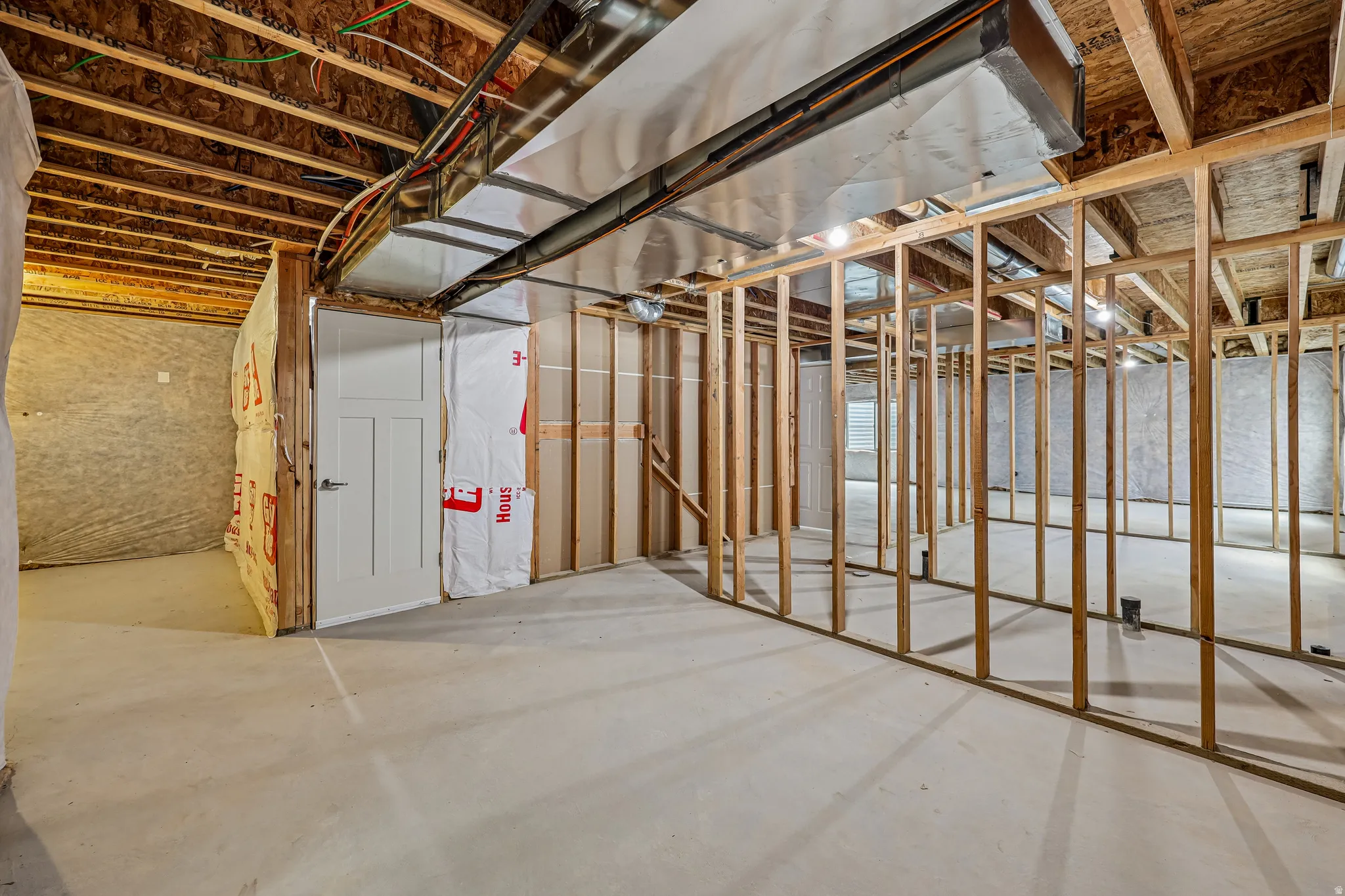 Unfinished lower level featuring exposed framing, concrete flooring, visible ductwork, and a paneled white door