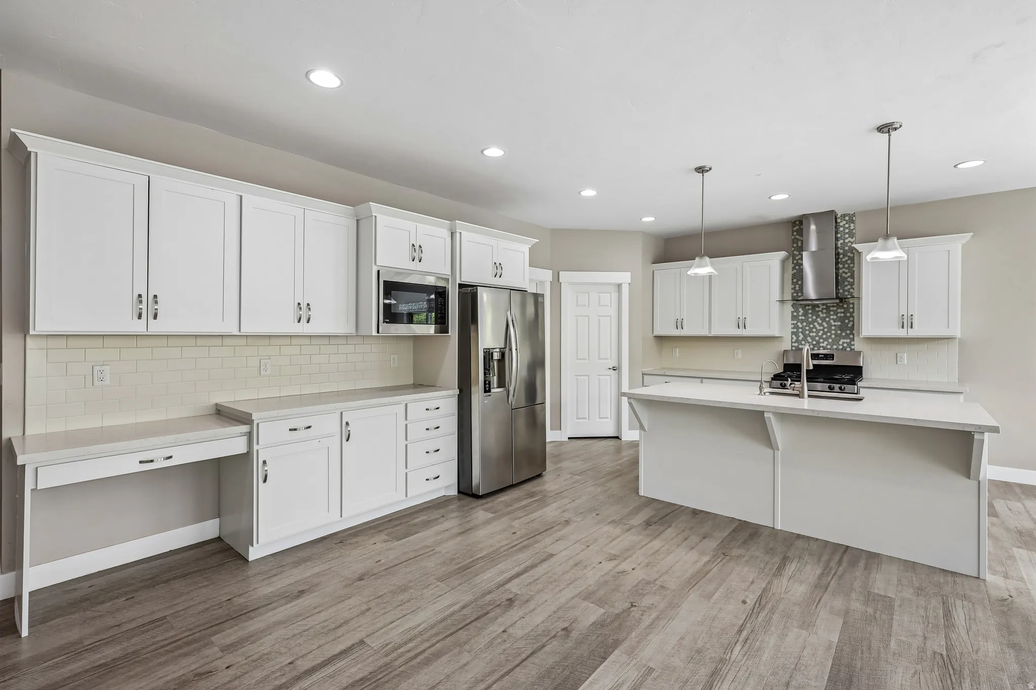 Open-concept kitchen featuring wood-finish flooring, white cabinetry, a built-in stainless steel microwave, a stainless steel refrigerator, and an island with pendant lighting