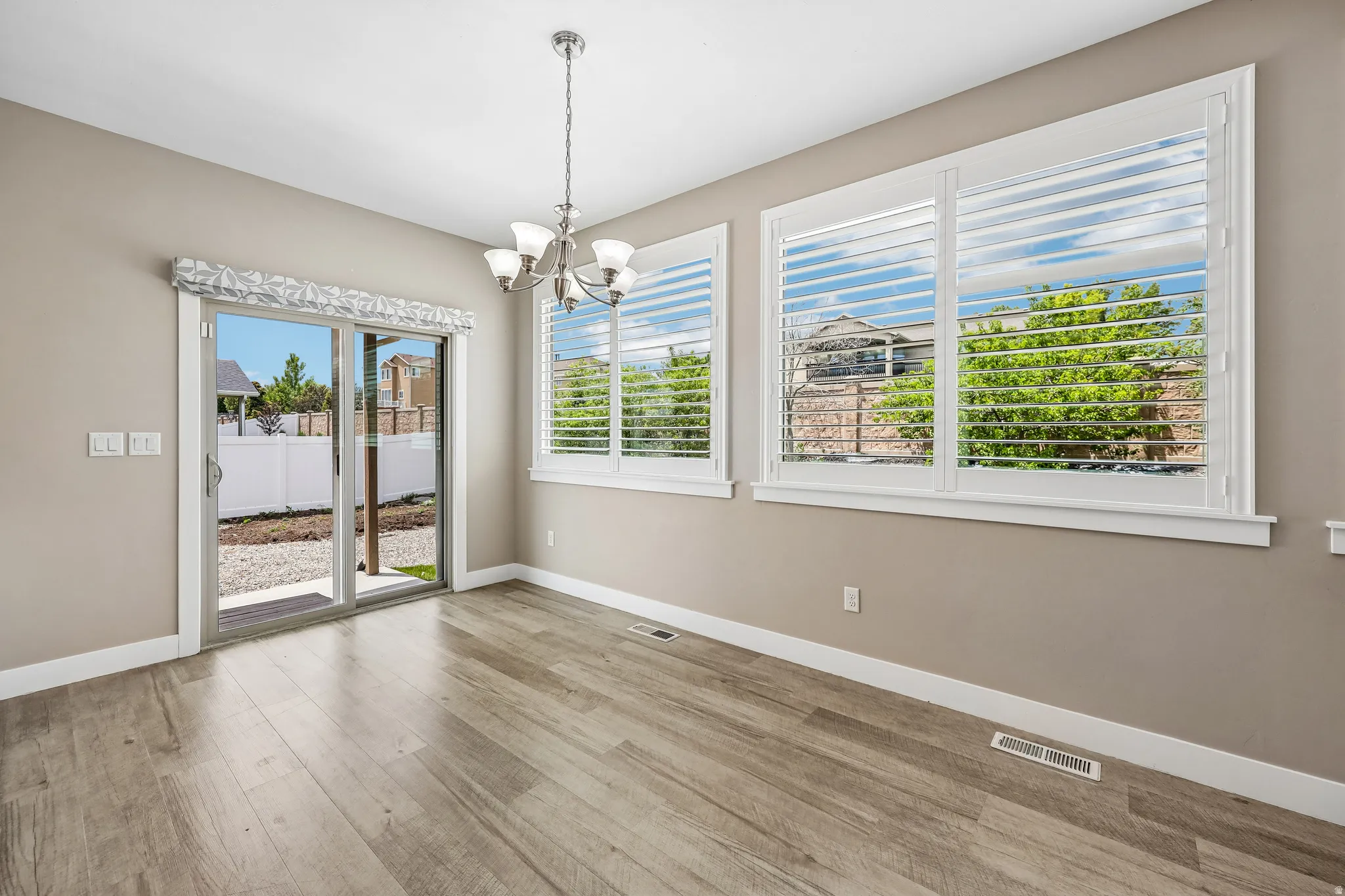 Bright interior space featuring wood-finish flooring, a contemporary chandelier, and large windows with plantation shutters