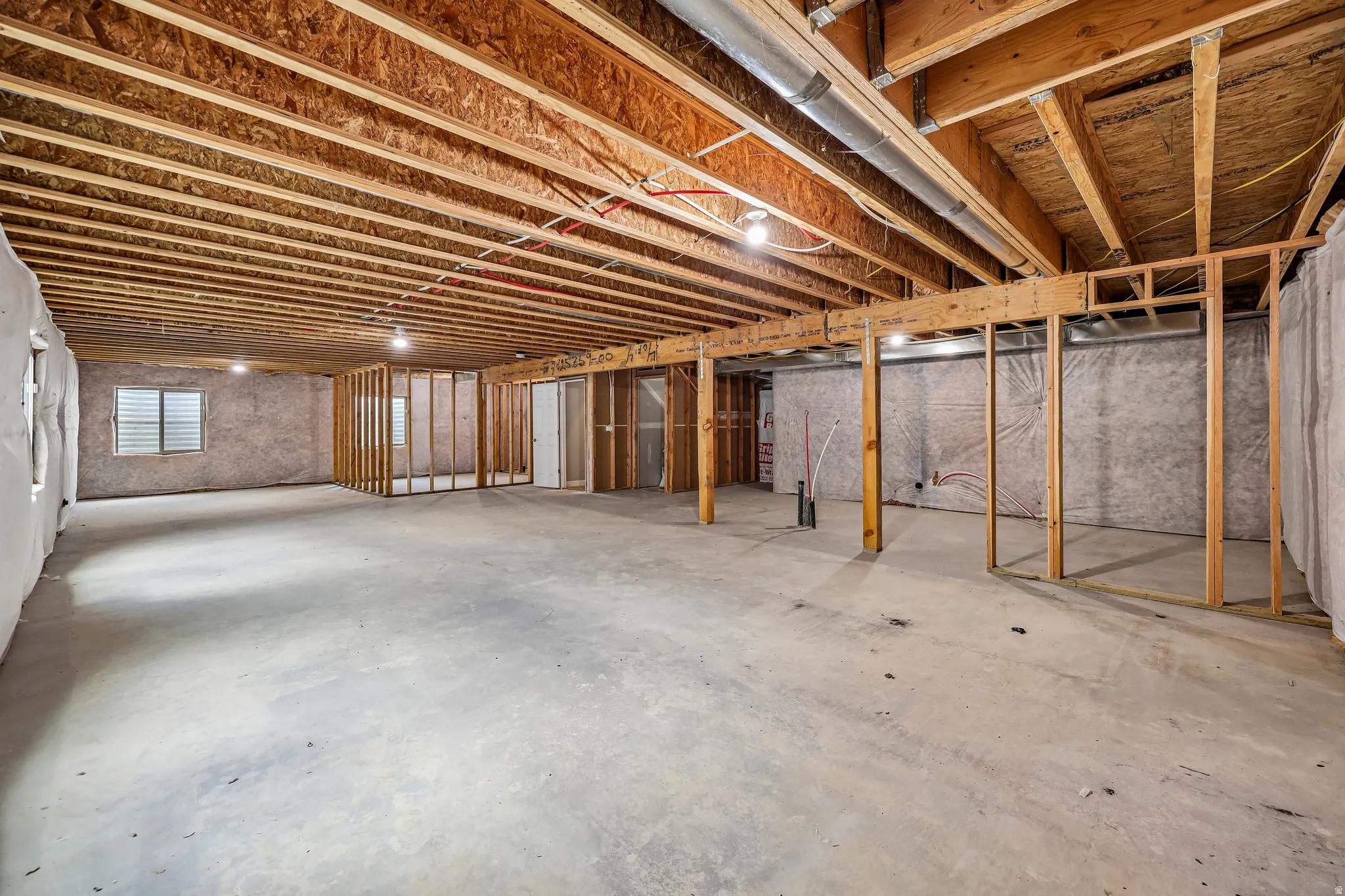 Expansive unfinished basement featuring a concrete floor, exposed wood ceiling joists, framed interior walls, and a window with blinds