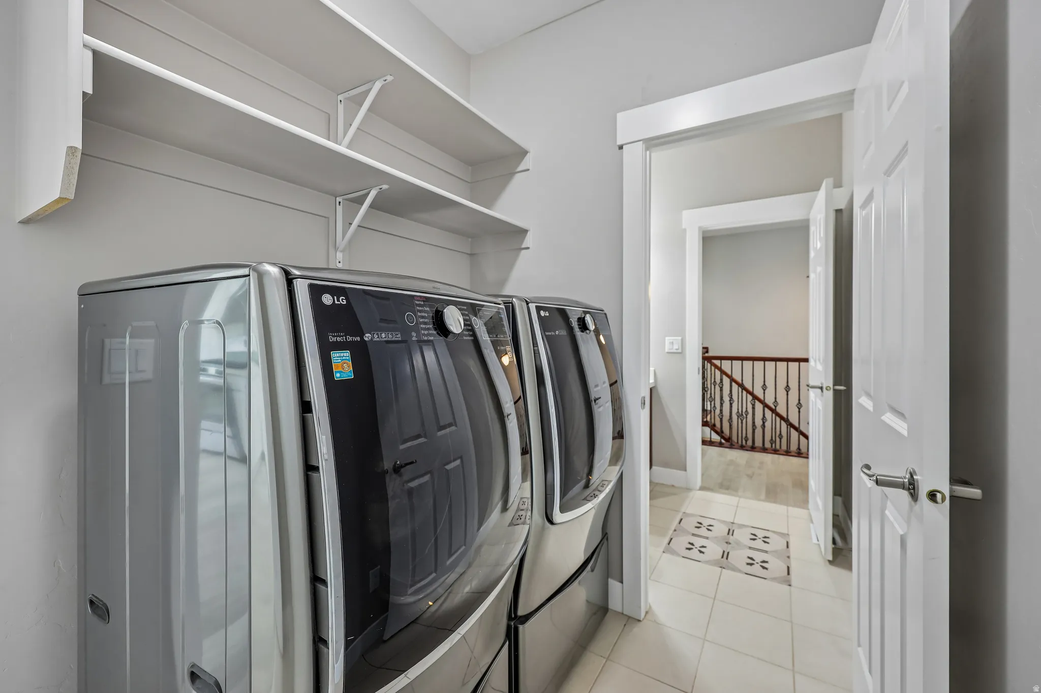 Dedicated laundry area featuring a side-by-side washer and dryer, open shelving, and light-toned tile flooring