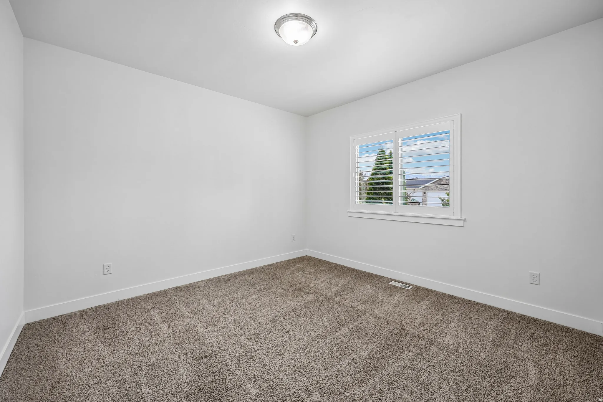 Carpeted room featuring white walls, a white trim window with plantation shutters, and a flush-mount ceiling light fixture