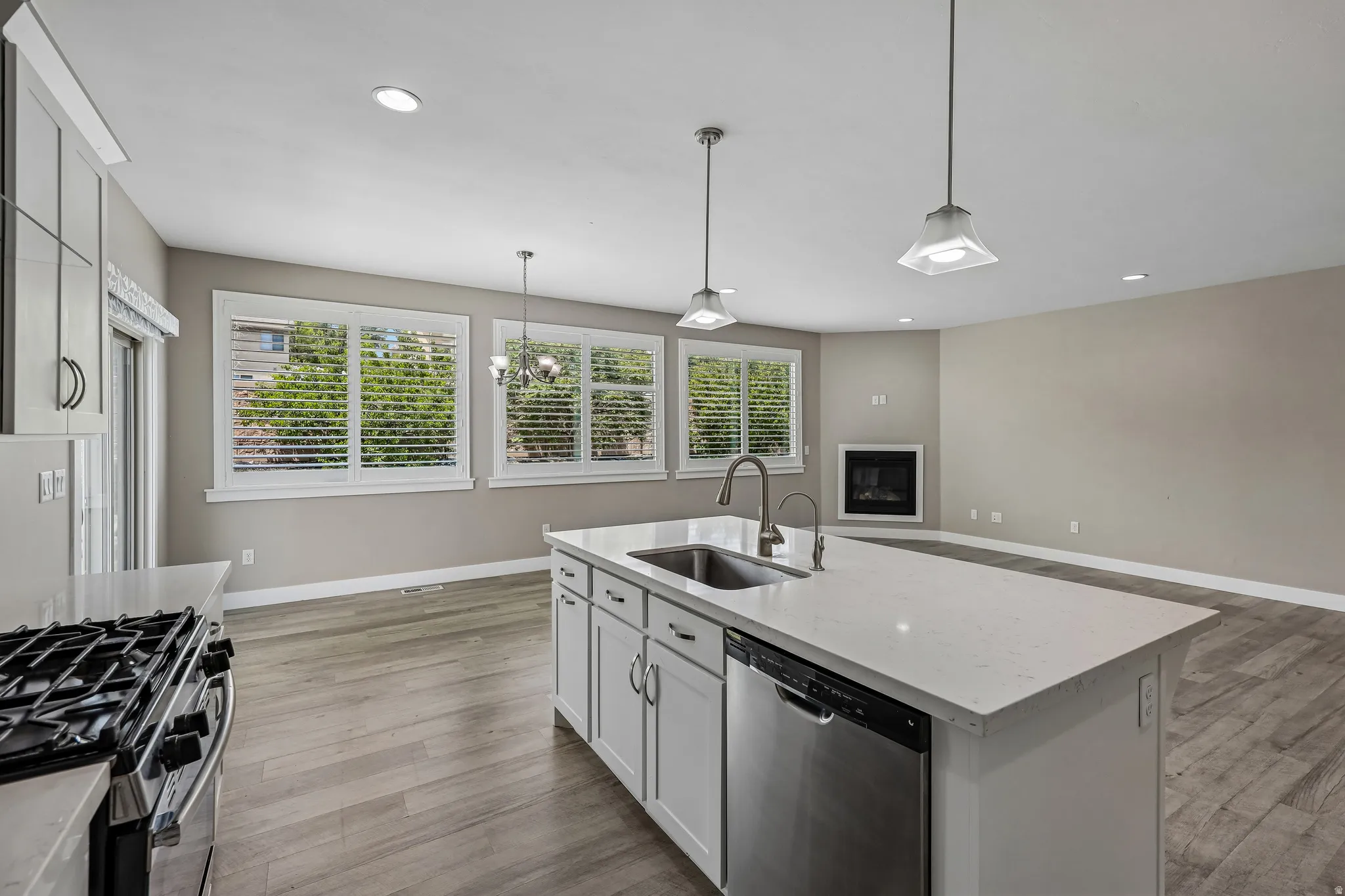 Open-concept living space featuring a central kitchen island with a built-in sink and dishwasher, white shaker cabinetry, and light-toned countertops