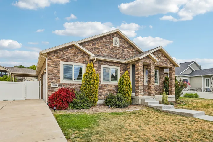 Stone veneer exterior featuring a covered front porch, concrete walkway, and attached garage