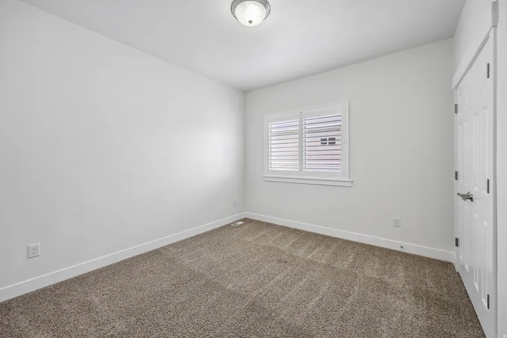 Carpeted room featuring a window with white plantation shutters, white trim, a flush mount ceiling light, and a paneled interior door