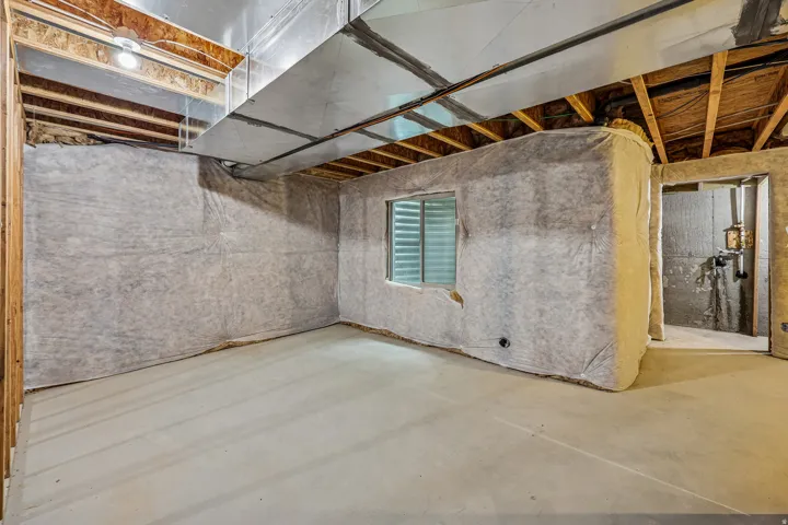 Unfinished basement space featuring exposed wood joists, a window with horizontal blinds, and a concrete floor