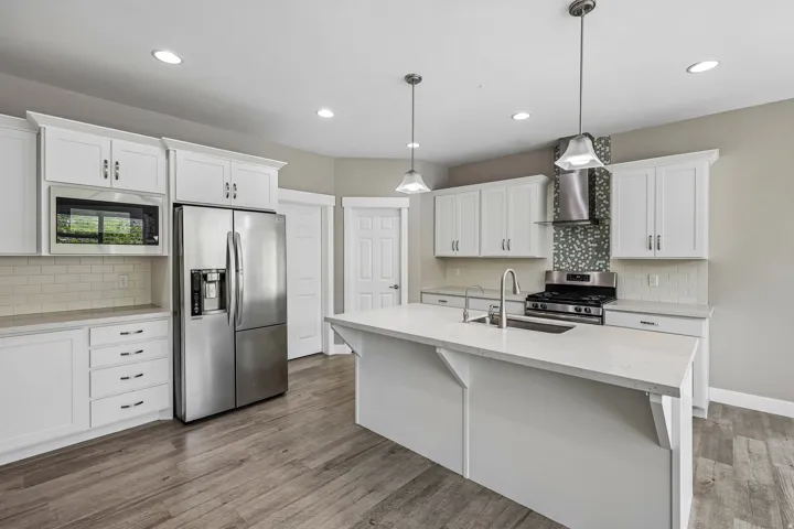 Modern kitchen featuring white shaker cabinetry, stainless steel appliances, a center island with sink and pendant lighting, wood-finish flooring, and a decorative tile backsplash