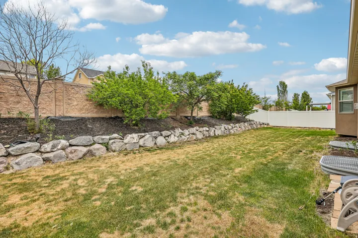 Expansive backyard featuring a rock retaining wall, mature trees, and a decorative concrete privacy fence