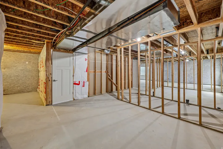 Unfinished lower level featuring exposed framing, concrete flooring, visible ductwork, and a paneled white door
