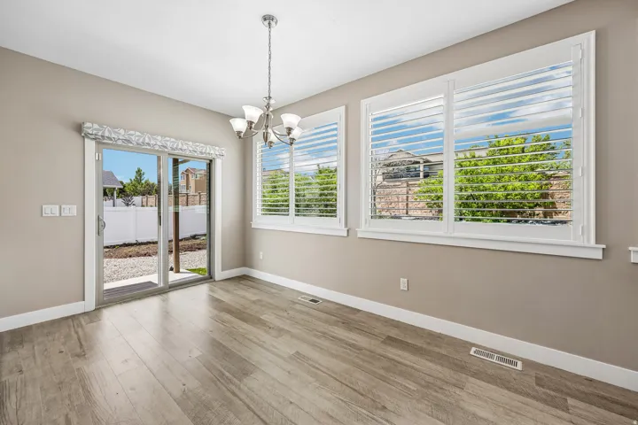 Bright interior space featuring wood-finish flooring, a contemporary chandelier, and large windows with plantation shutters