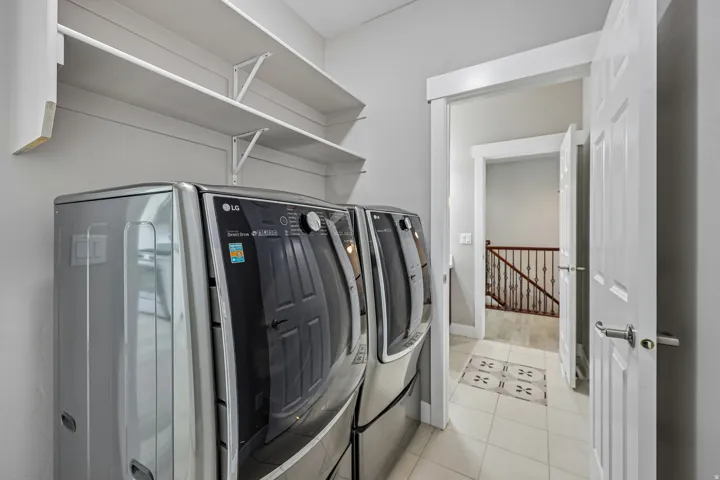 Dedicated laundry area featuring a side-by-side washer and dryer, open shelving, and light-toned tile flooring