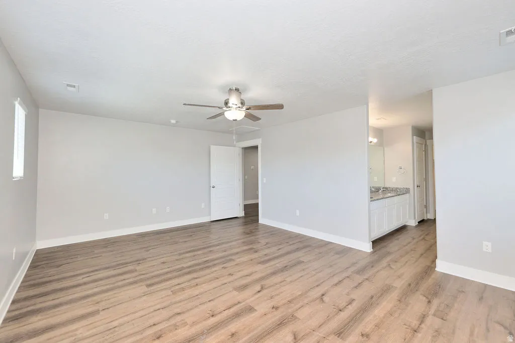 Spacious room featuring wood-finish flooring, light gray walls, a ceiling fan with integrated lighting, and white trim