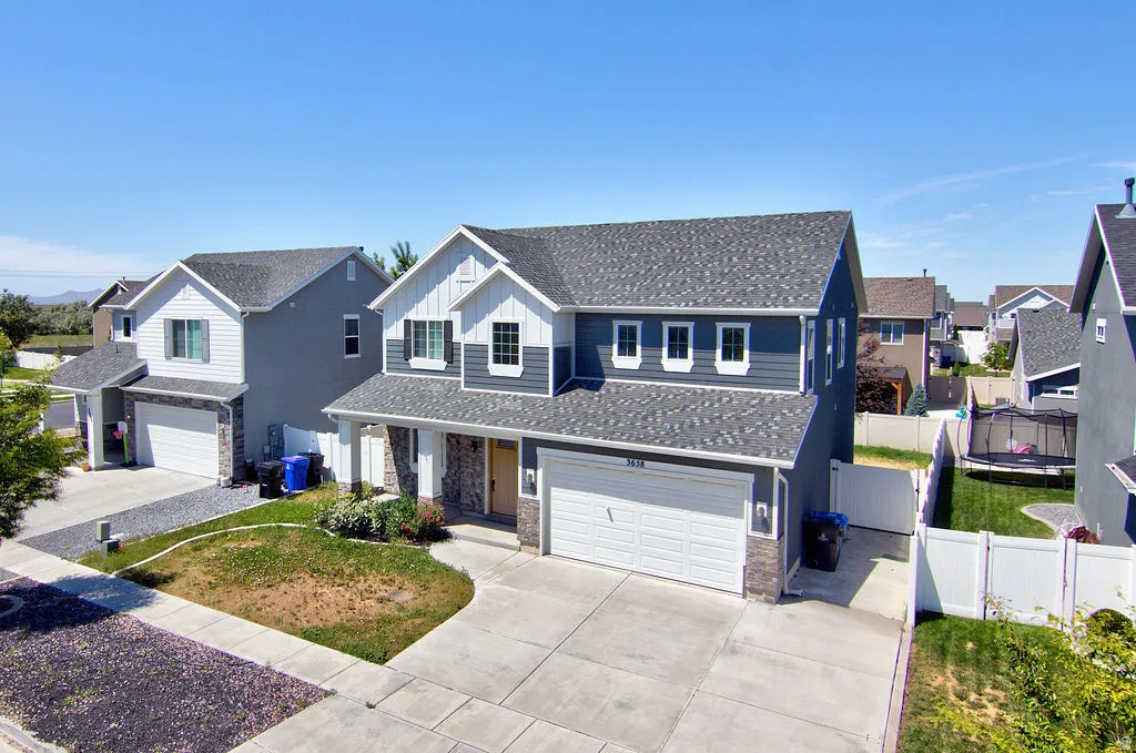 Two-story residence featuring a two-car garage, stone and siding exterior, front porch entry, and a fenced backyard