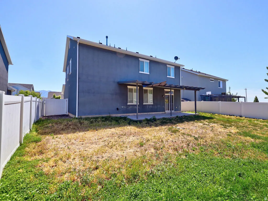 Rear exterior featuring a concrete patio with an attached pergola structure, a sliding glass door, and multiple windows