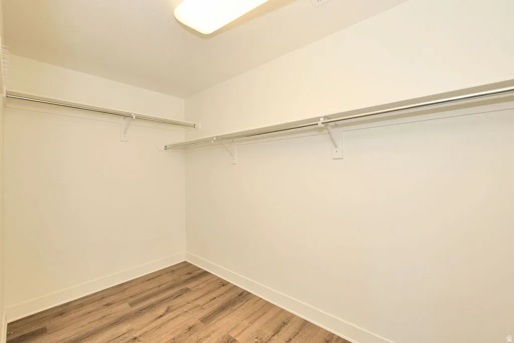 Spacious walk-in closet featuring wood-finish flooring, white walls, white baseboards, and built-in white wire shelving and hanging rods