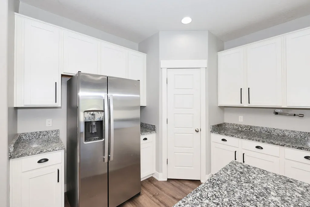 Contemporary kitchen featuring white shaker cabinetry, stainless steel side-by-side refrigerator, granite countertops, and wood-finish flooring