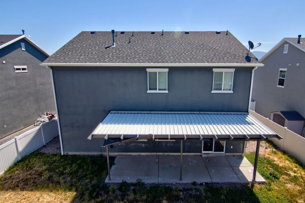 Rear exterior featuring a covered patio with a concrete slab, dark gray stucco siding, and a shingled roof
