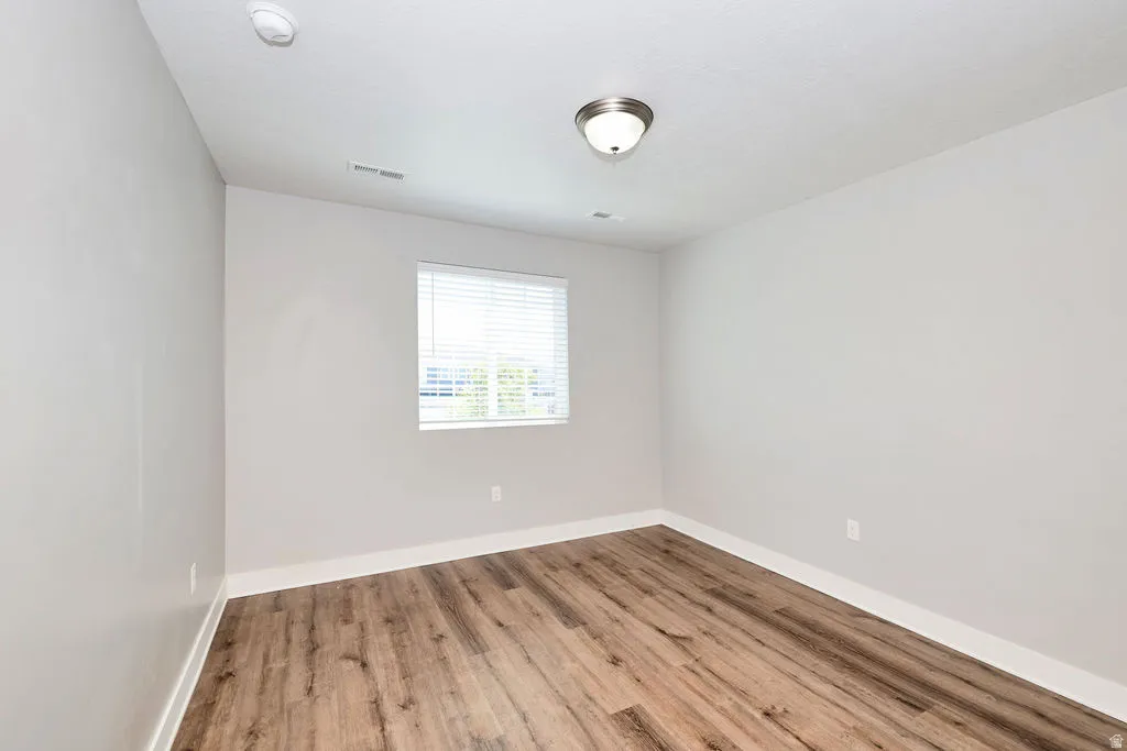 Room featuring wood-finish flooring, light grey painted walls, white baseboards, and a single window with horizontal blinds