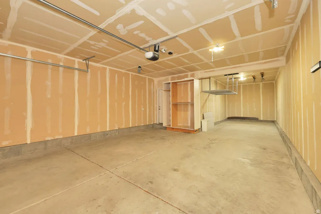 Spacious garage featuring a durable concrete floor, exposed drywall walls, built-in shelving, an automatic garage door opener, and overhead storage racks