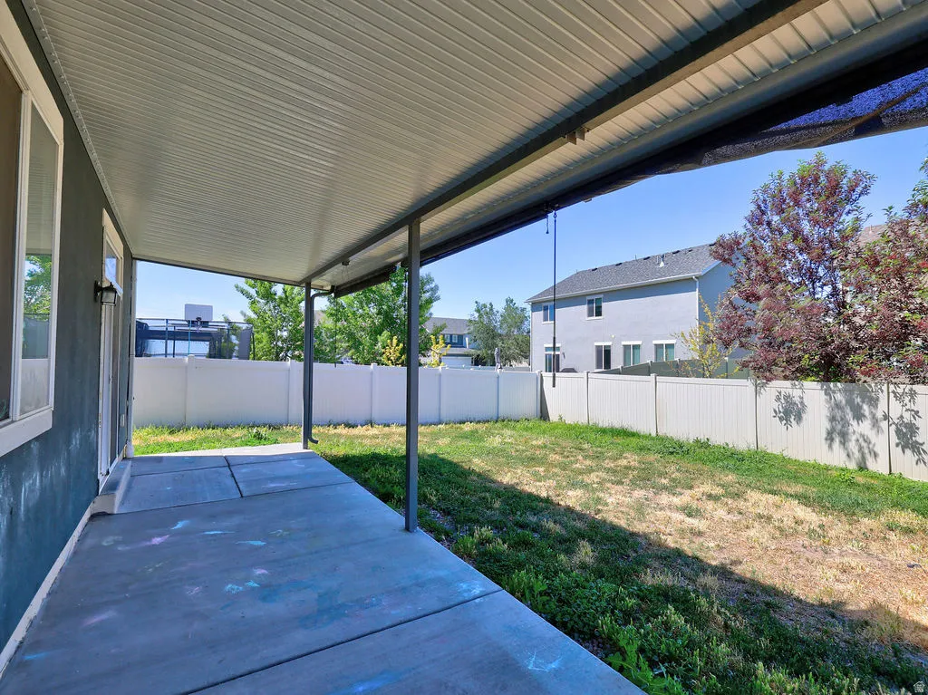 Covered concrete patio extending to a fenced backyard with natural grass and mature landscaping