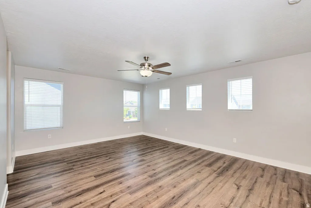 Spacious room featuring wood-finish flooring, light gray walls, and multiple windows with white blinds