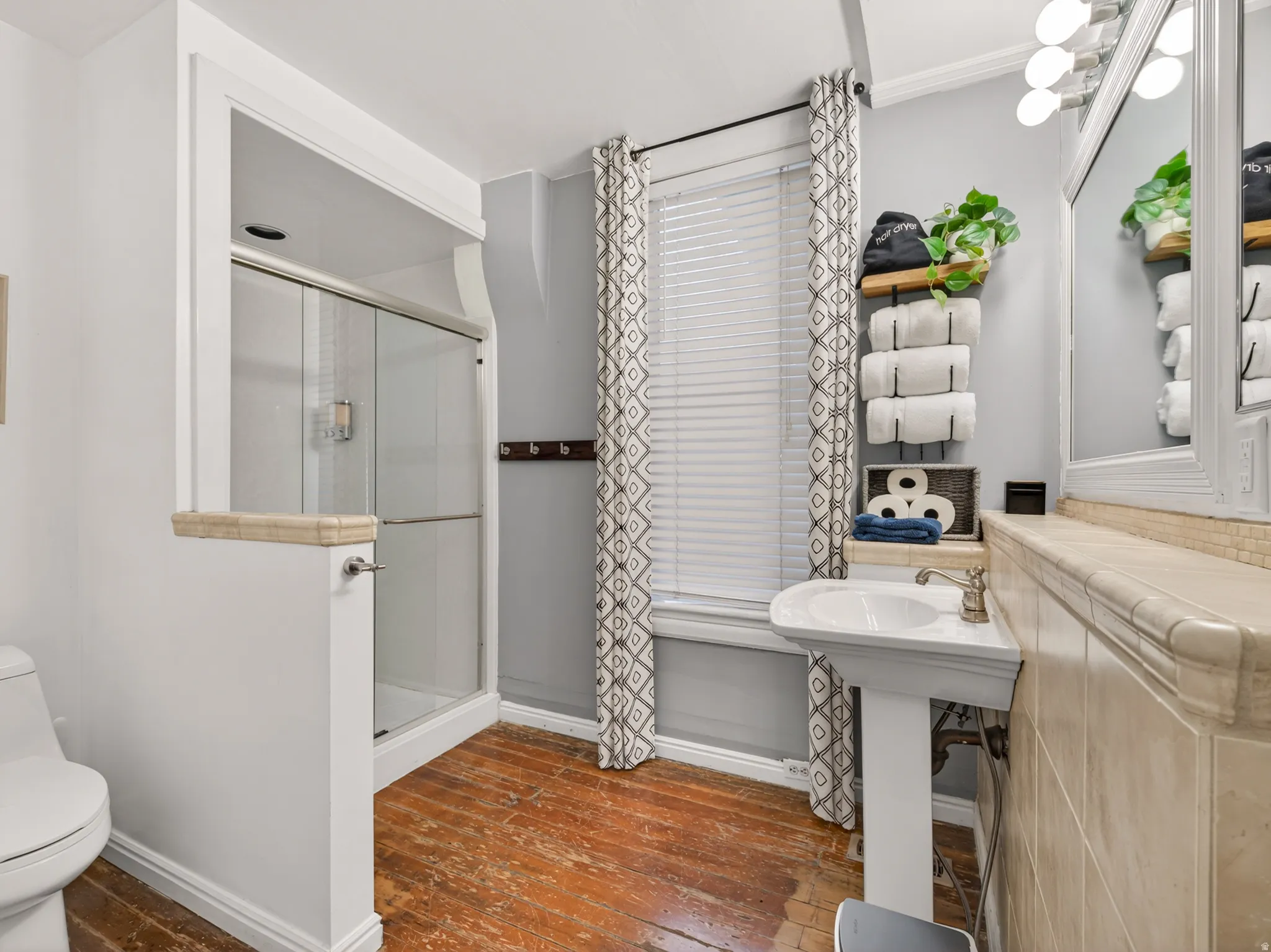 Bathroom featuring a pedestal sink, a glass-enclosed shower, wood-finish flooring, a toilet, and a tiled vanity area