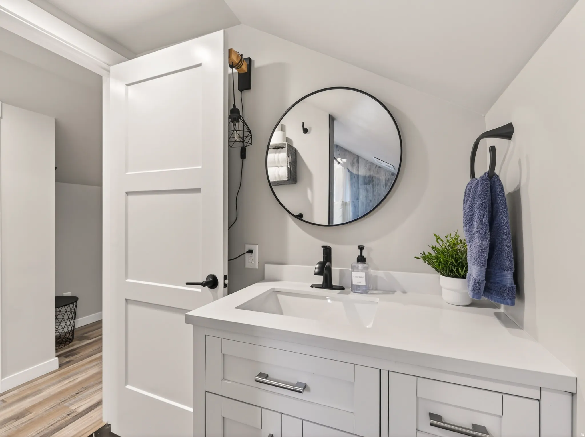 Vanity with an integrated rectangular sink, white countertop, matte black faucet, and wood-finish flooring
